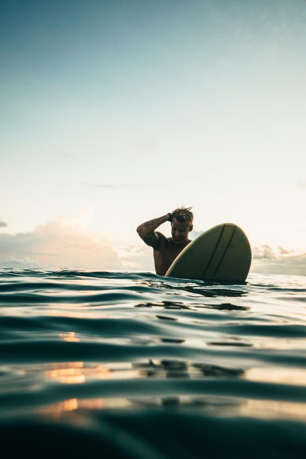 A man paddleboarding across calm water at sunset — unhurried, deliberate time, the same quality a real men's-health visit is built around