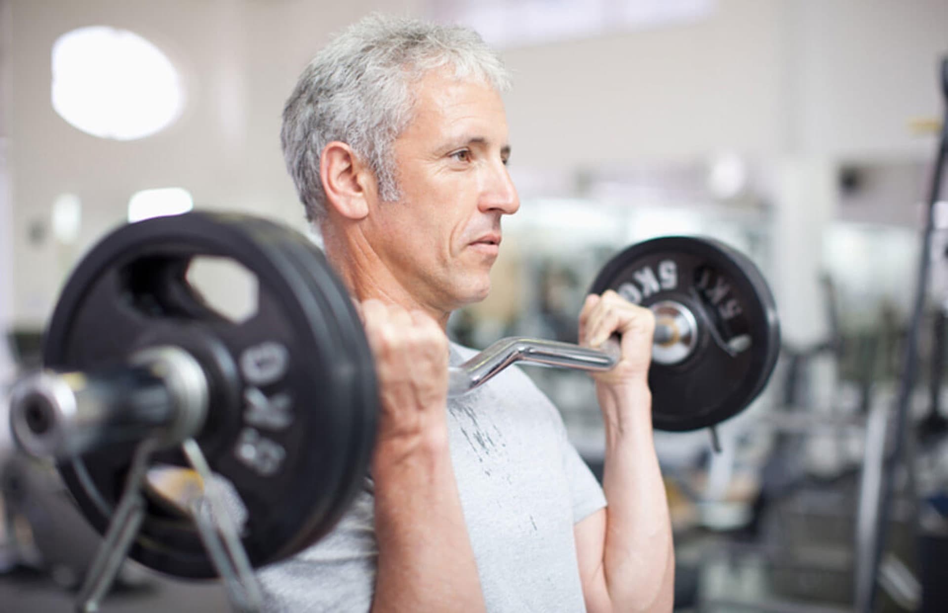 Silver-haired mature male doing barbell curls — a man over 40 keeping the strength signals working while his testosterone profile is properly diagnosed