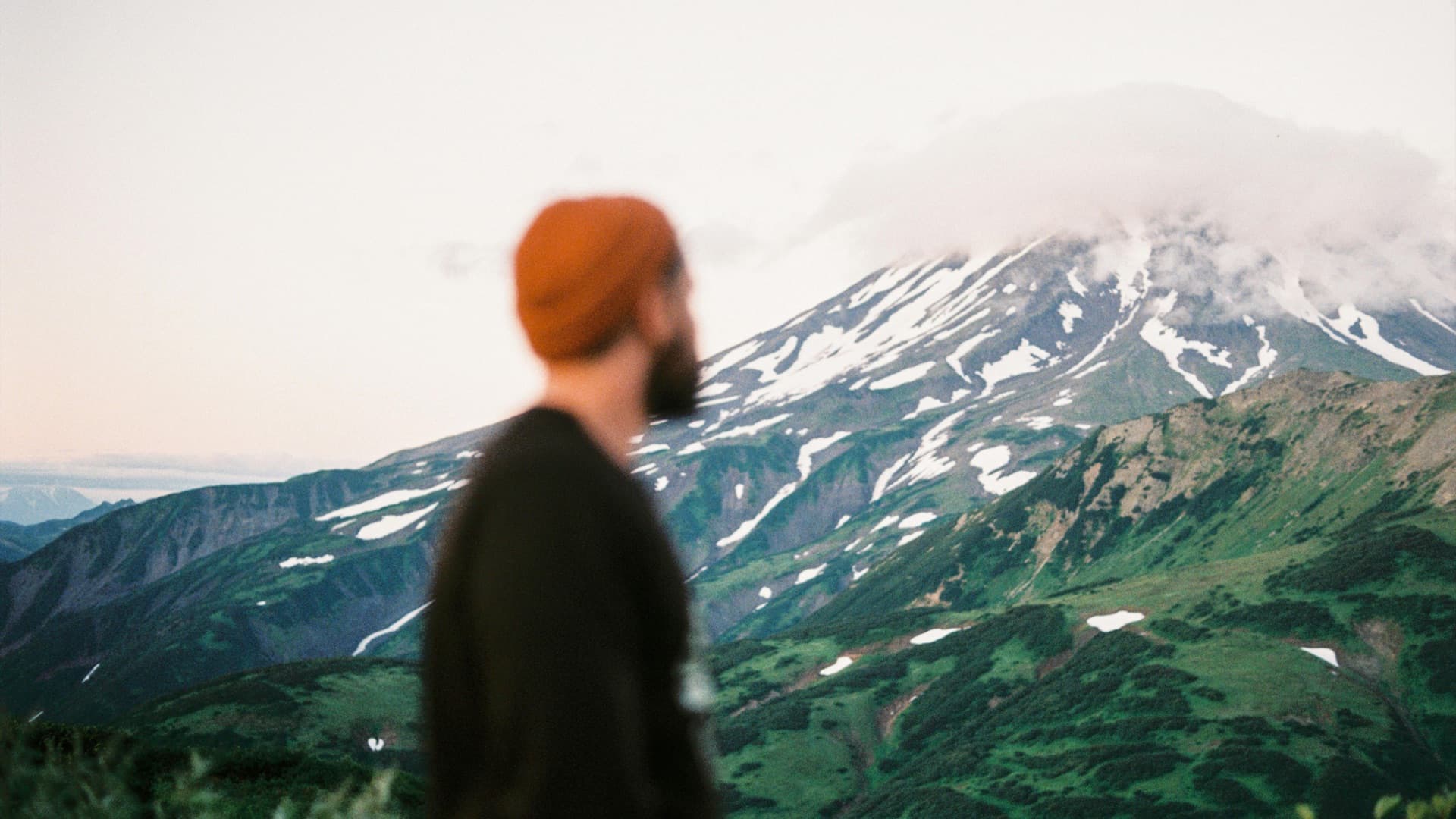 Bearded man in the foreground looking out toward a snow-capped mountain vista — the contemplative frame for the question of why we age, and what's actually modifiable about the trajectory