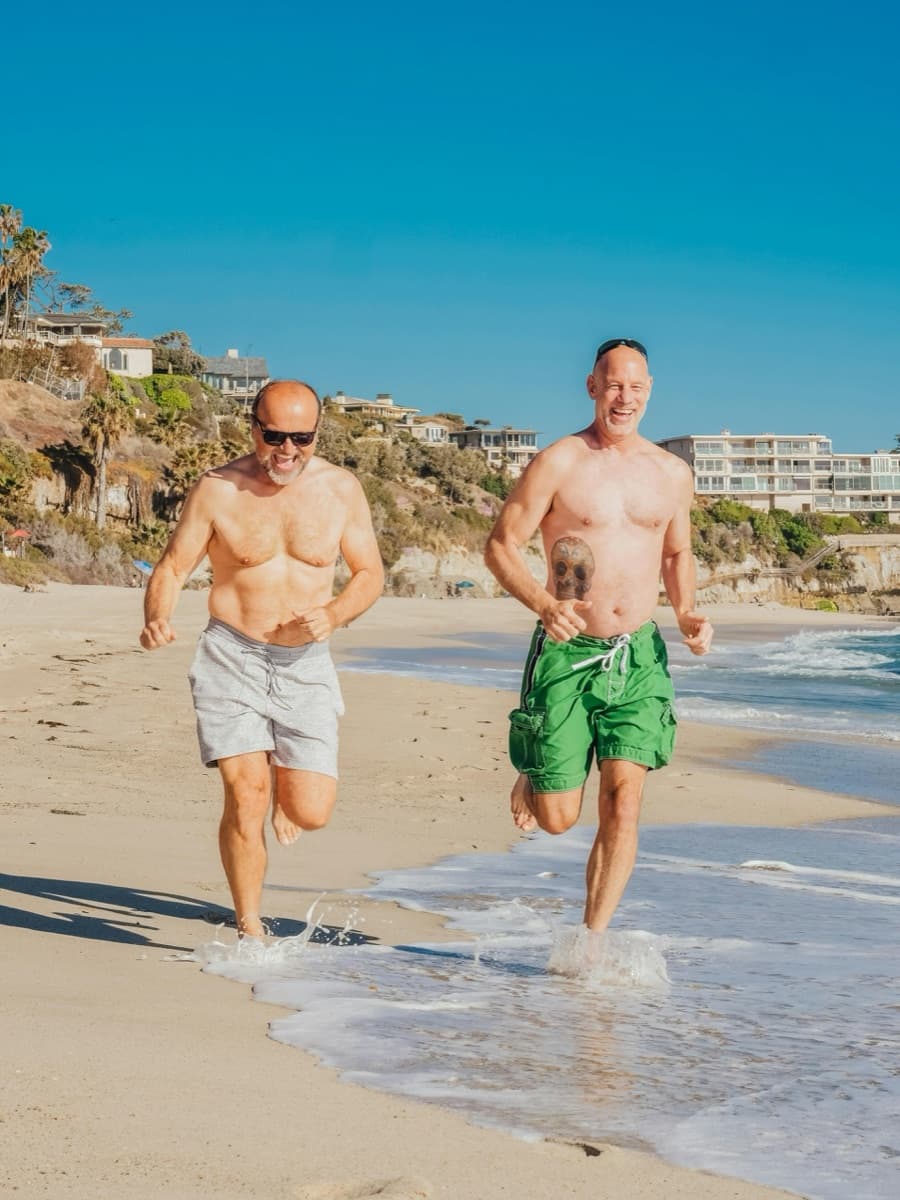Two men in mid-life running along the beach — the everyday function testosterone replacement is meant to restore, not exceed