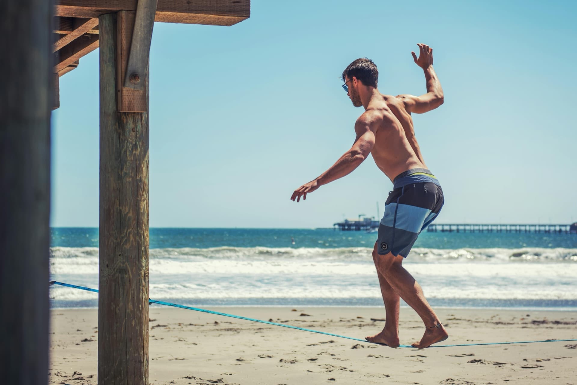 A man holding his balance on a slackline strung between two anchors at the beach — the same kind of tensioned feedback loop the brain and testicles maintain to hold testosterone steady