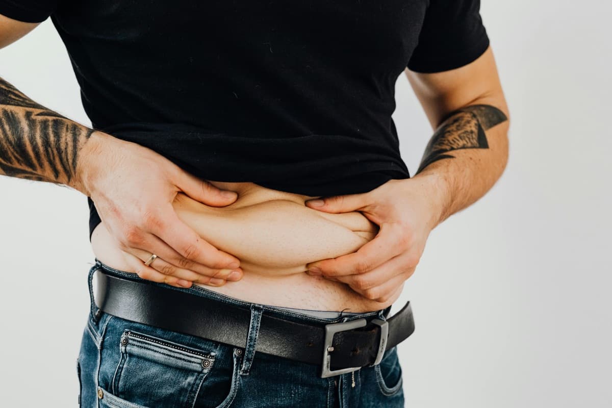 Man pinching his abdominal weight with both hands — the stubborn middle-section weight that doesn't move with the same diet that worked five years ago